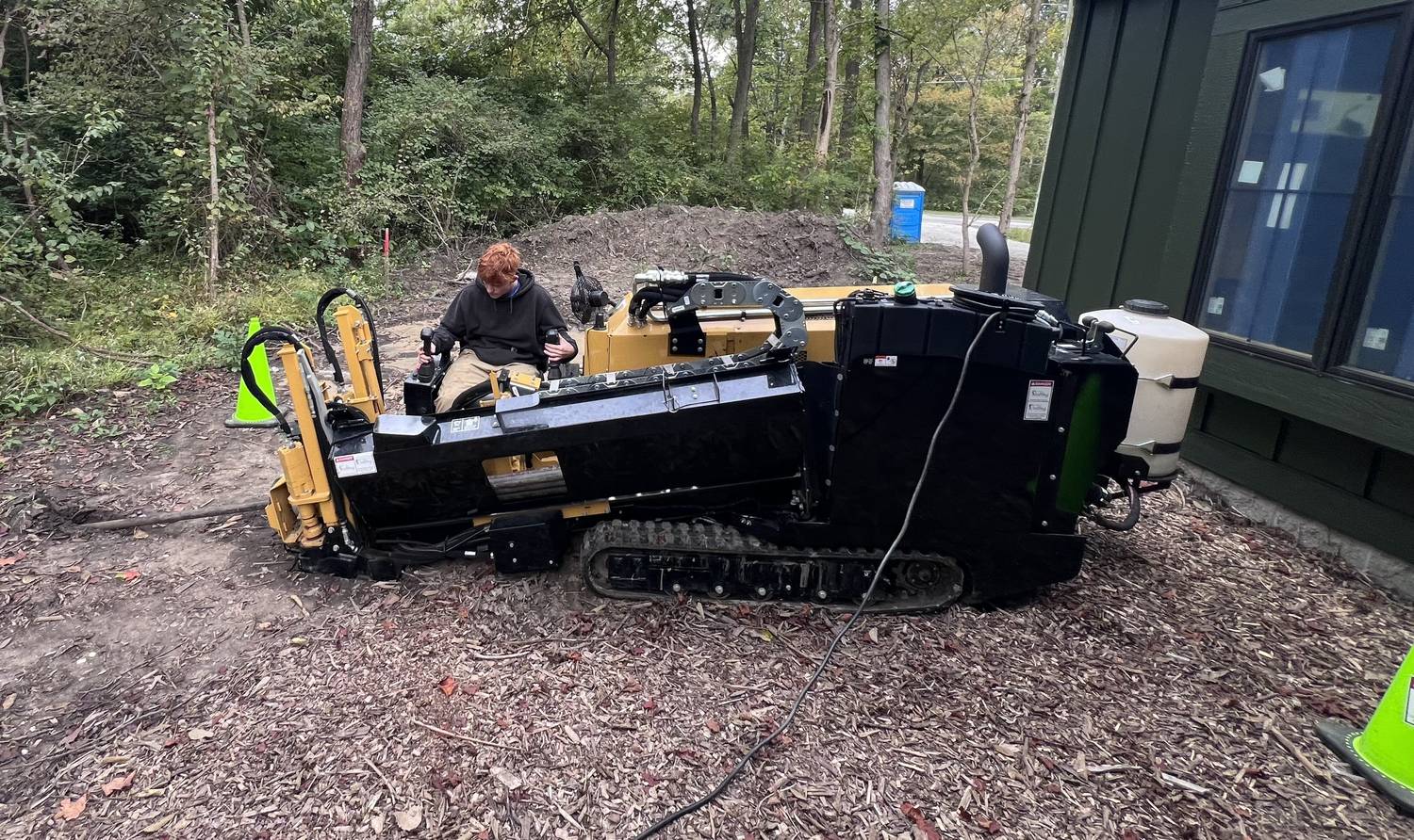 A directional boring rig running a bore beside a house, operator at the controls